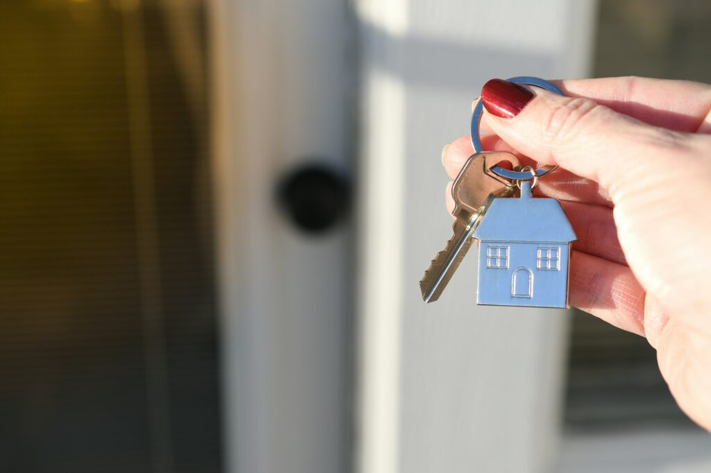 Female realtor's or homeowner hand holding a set of keys outside front door during golden hour.